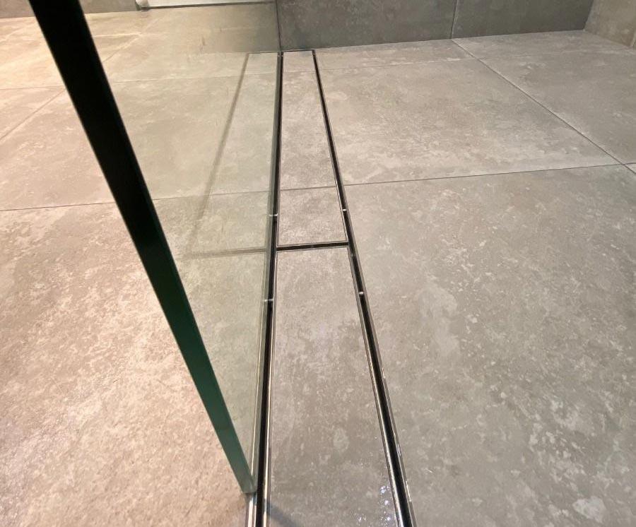 Where should a linear shower grate be placed?